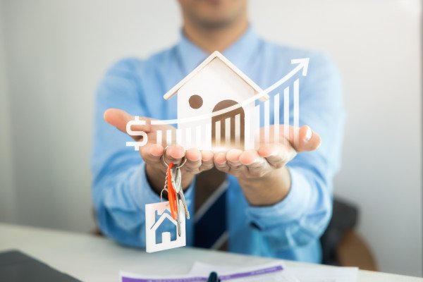 Person mit ausgstreckten Händen, Grafik mit Haus und einem steigenden Graph in den Händen platziert