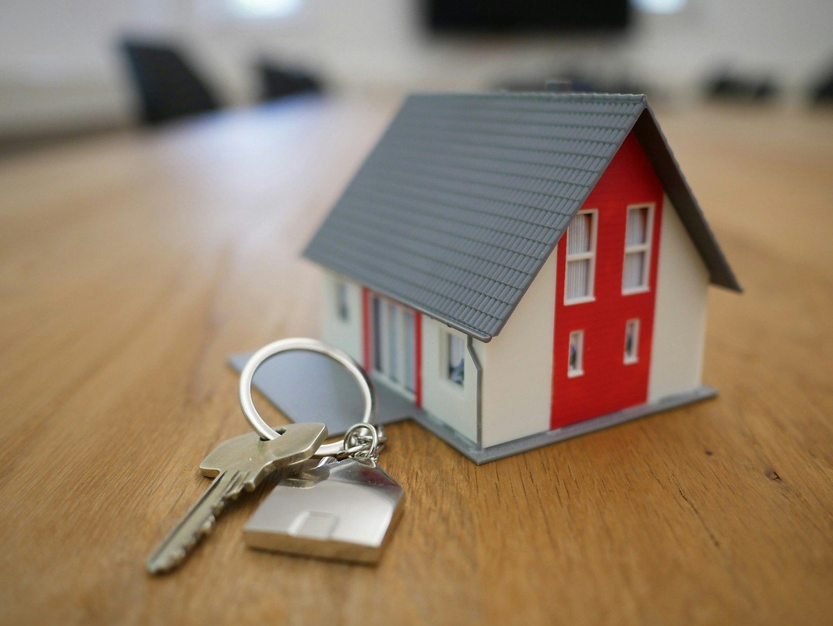 Miniaturhaus und Hausschlüssel liegen nebeneinander auf einem Tisch